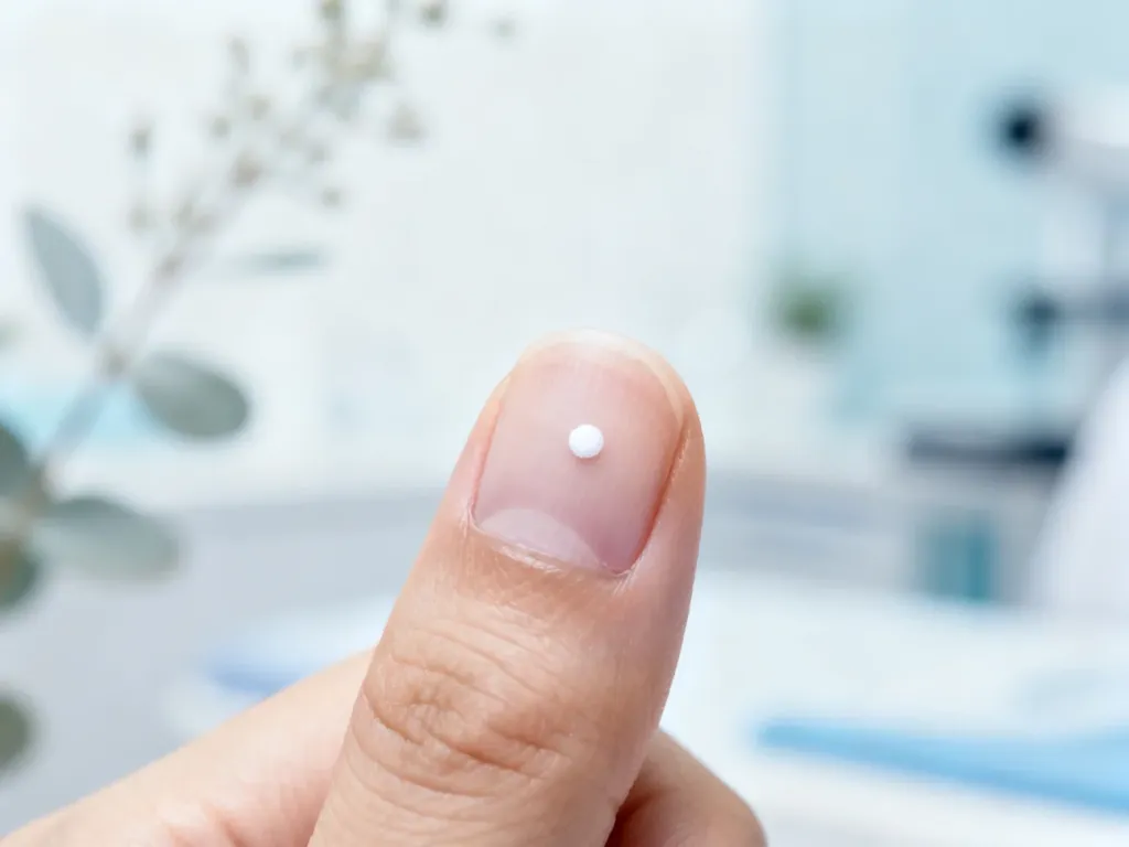 Zbliżenie na paznokieć z widoczną białą plamką na tle gabinetu dermatologicznego w chłodnej, medycznej tonacji.